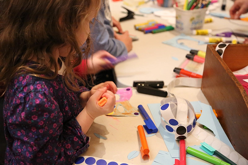 Child creating craft artwork with markers and paper at a table.