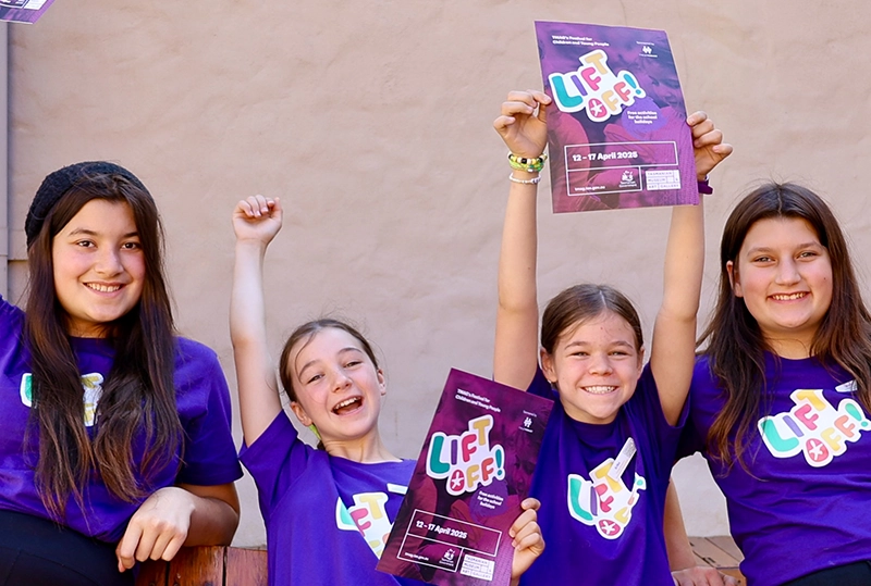 Children holding “Lift Off!” festival posters and smiling.