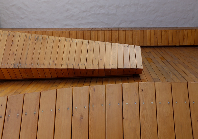 Angled wooden bench and seating inside a gallery space.