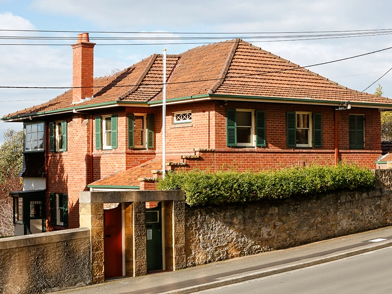 Historic red-brick house museum with green shutters and tiled roof on a sloping street.