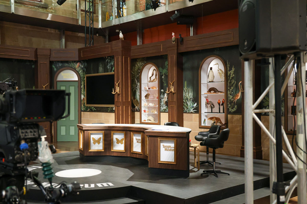 Museum studio set with display cabinets, desk and filming equipment.