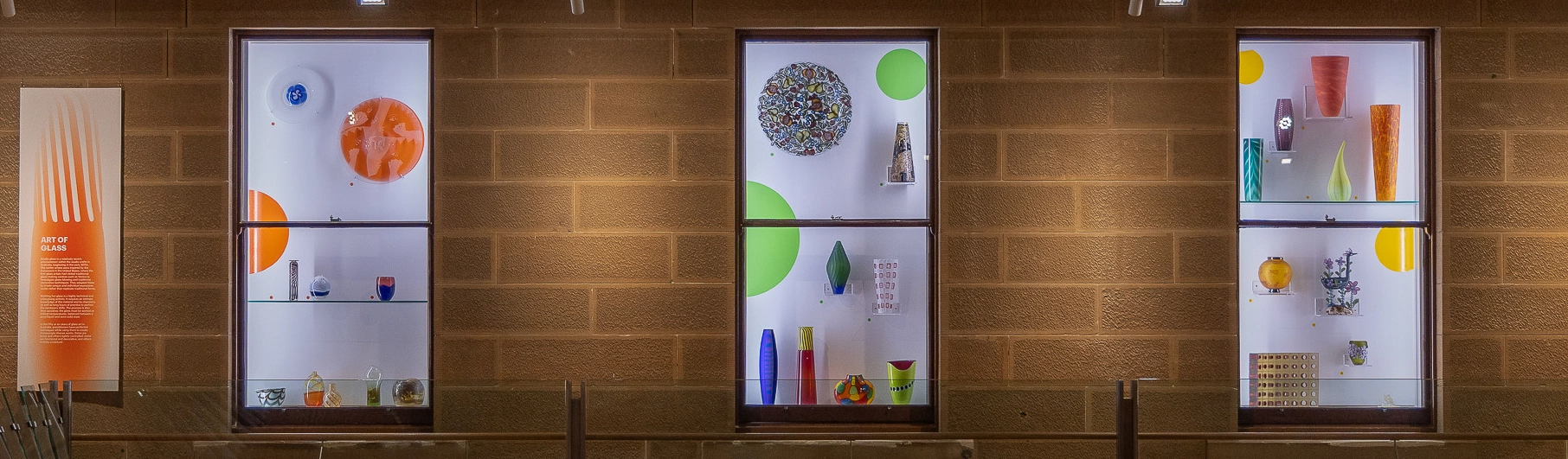 Illuminated display windows featuring colourful glass artworks.