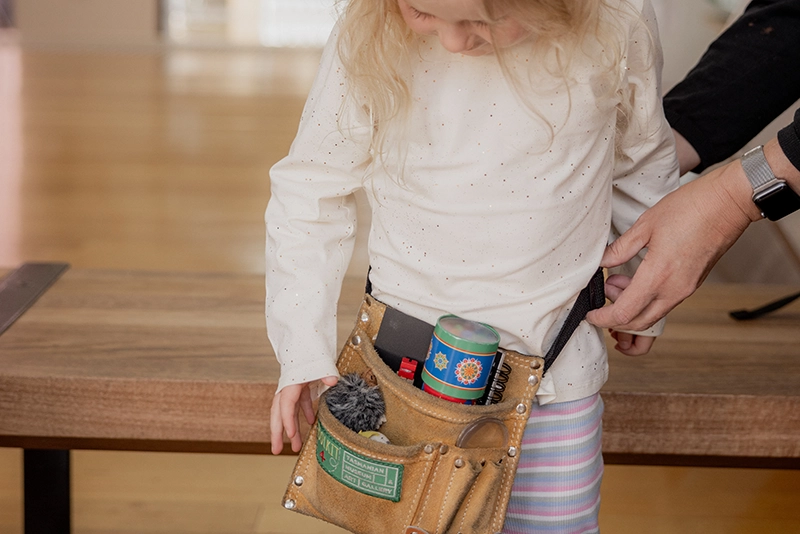 Child wearing a museum activity belt filled with tools and toys.