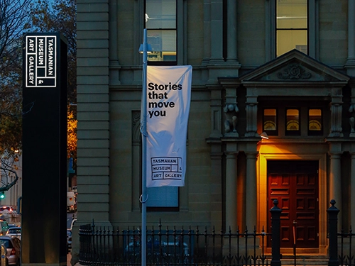 Evening view of the museum entrance with a lit doorway and a banner reading “Stories that move you.”