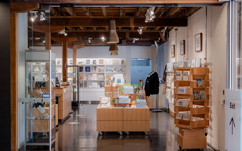 Museum shop interior with wooden shelving, books, gifts and display cabinets under exposed timber beams.