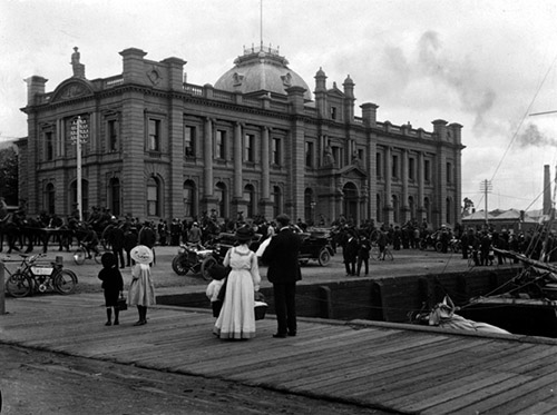 Historic waterfront scene with early 20th-century crowd outside TMAG building.