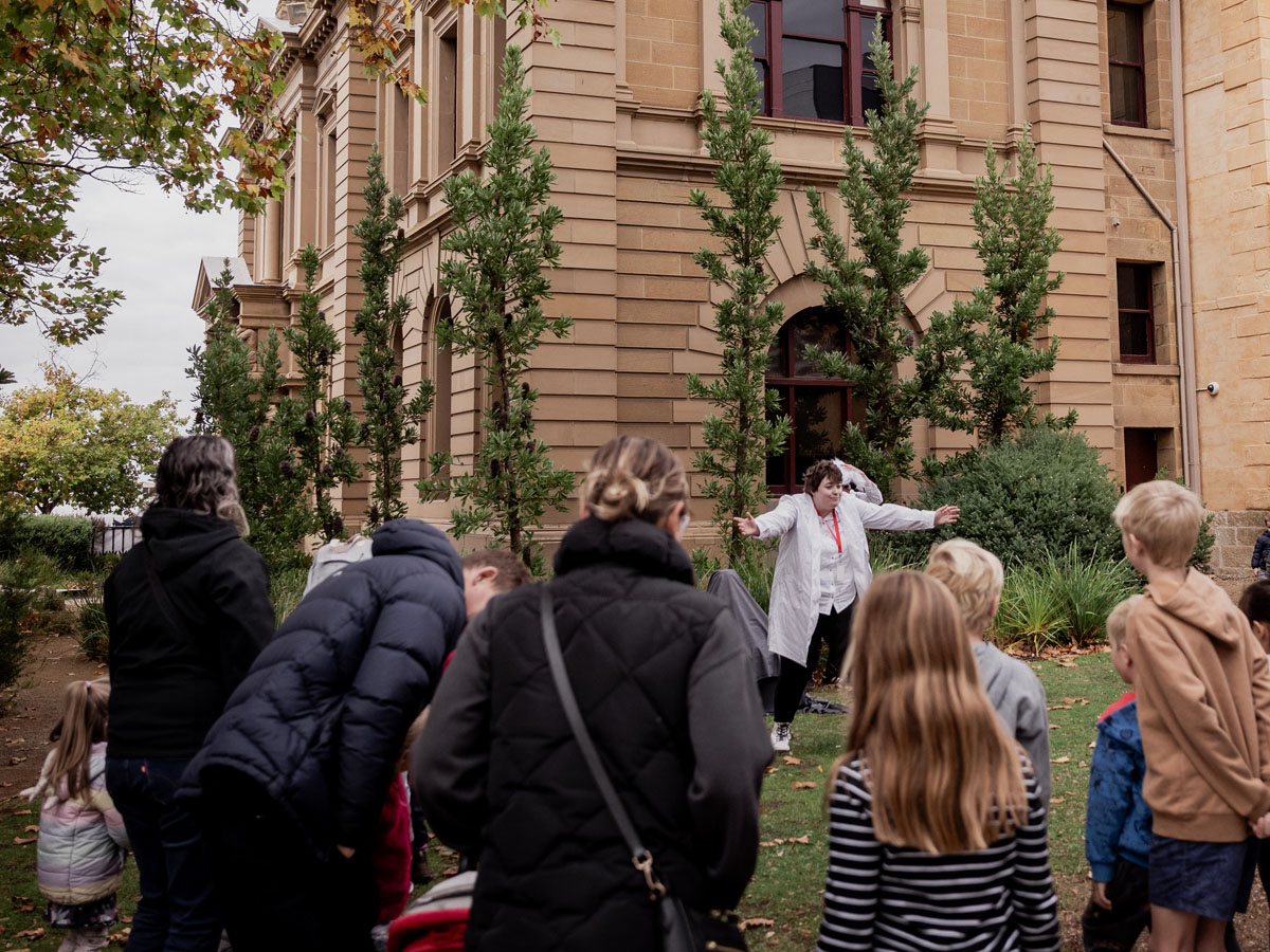 Museum guide leading a group of adults and children outside a historic building.