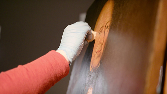 Image of gloved hand cleaning a colonial-era portrait of a man