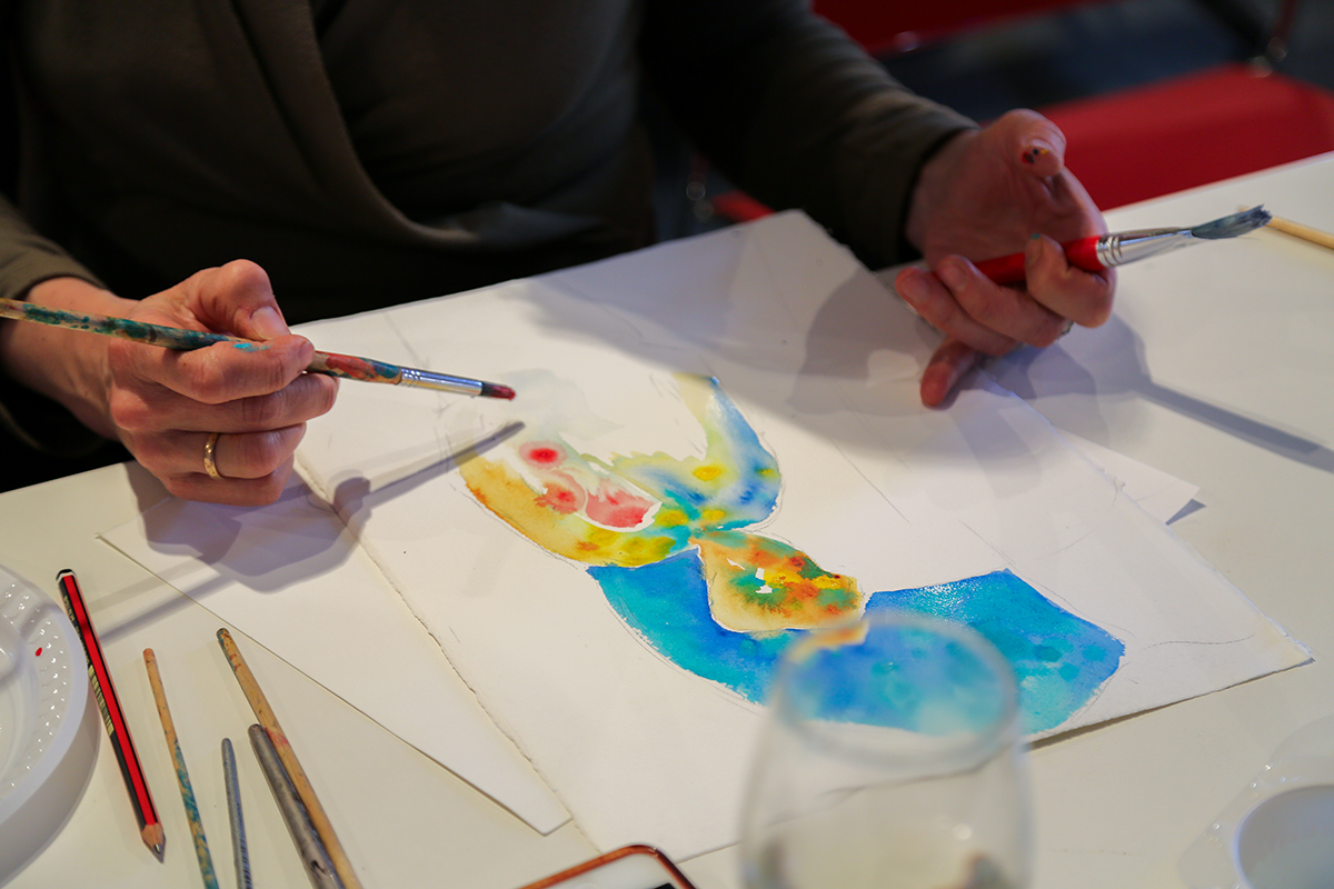 Person painting a colourful artwork with watercolours at a table.